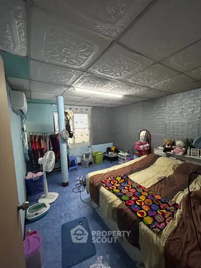 Cozy bedroom with colorful decor and unique ceiling tiles, featuring a fan and ample storage space.
