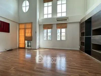 Spacious living room with high ceilings and wooden flooring, featuring large windows for natural light.