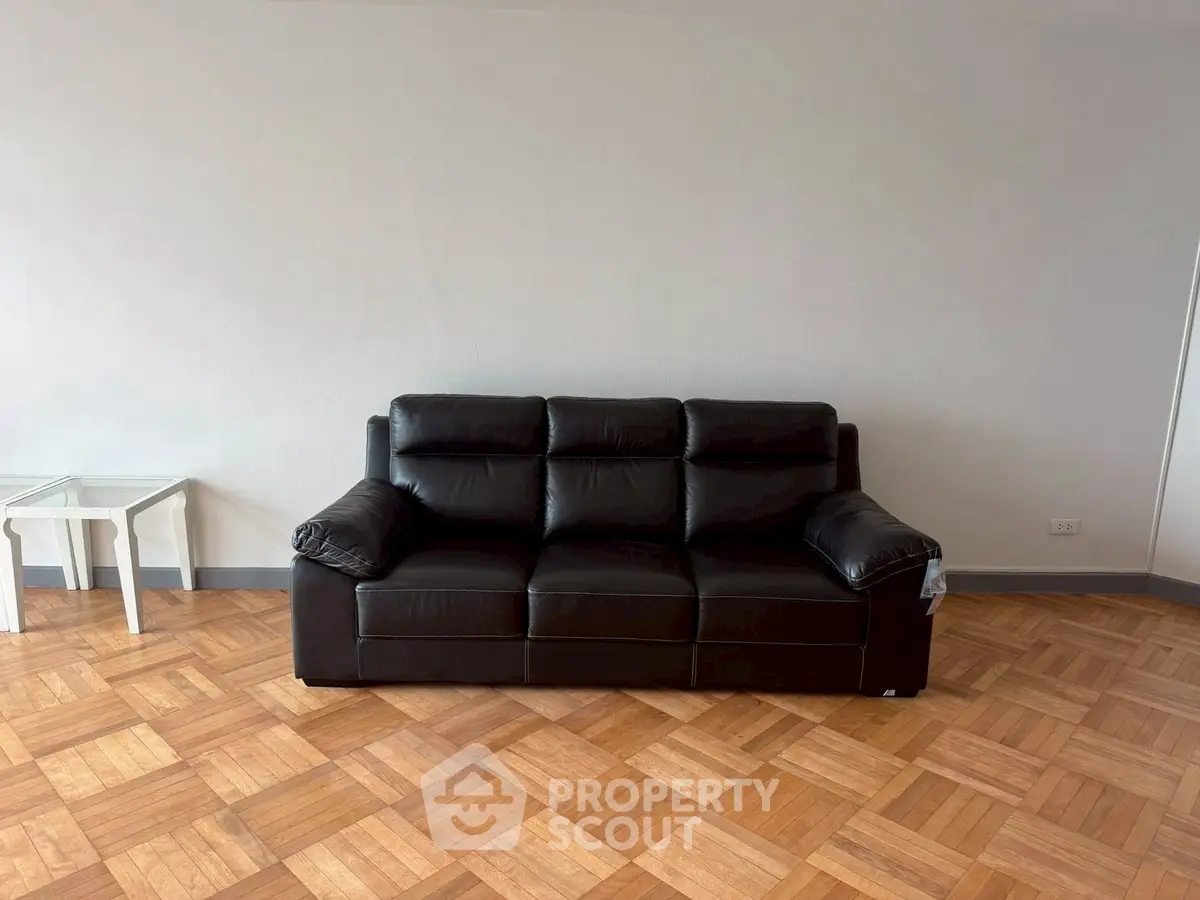 Spacious living room with elegant black leather sofa and parquet flooring.