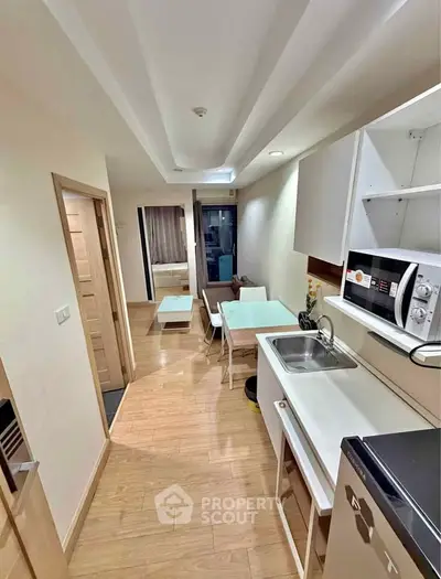 Modern compact apartment with open kitchen and cozy living area, featuring sleek appliances and wooden flooring.