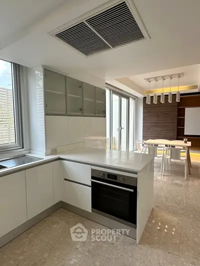 Modern kitchen with sleek white cabinetry and open layout leading to dining area.