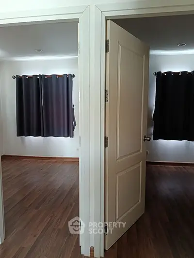 Spacious interior with two adjacent rooms featuring elegant wooden flooring and dark curtains.