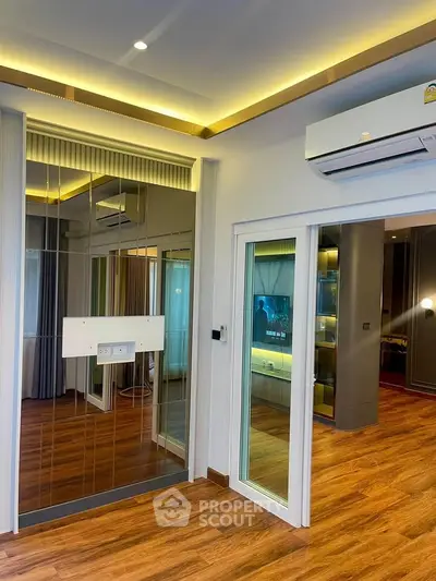 Modern living room with wooden flooring, mirrored wall, and air conditioning unit.
