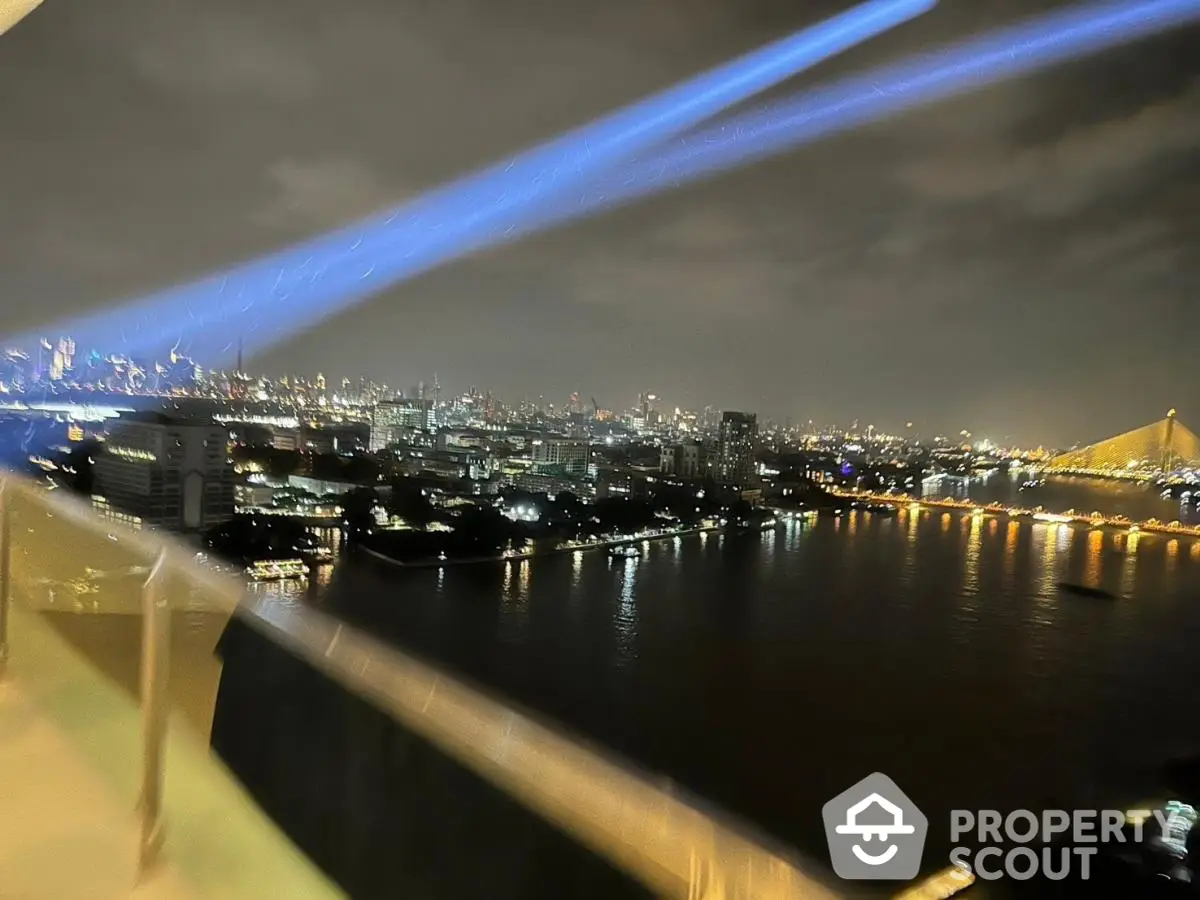 Stunning cityscape view from high-rise balcony overlooking river and illuminated bridge at night.