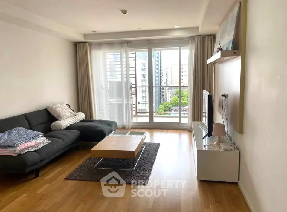 Modern living room with large windows and city view, featuring sleek furniture and wooden flooring.