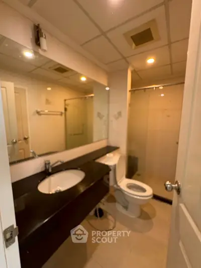 Modern bathroom with sleek fixtures and large mirror, featuring a spacious shower area.