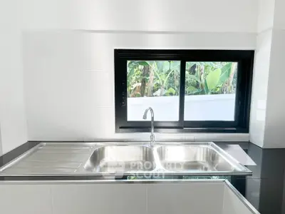 Modern kitchen with sleek stainless steel sink and large window view.