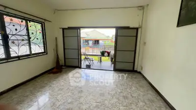 Spacious living room with sliding doors opening to a garden view, featuring tiled flooring and decorative window grills.