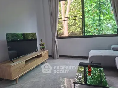 Modern living room with large window and stylish furniture overlooking lush greenery.