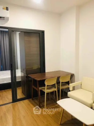 Modern apartment interior with sliding glass door, wooden flooring, and cozy furniture setup.