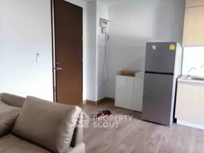 Modern apartment interior with sleek kitchen and cozy living area featuring a stylish sofa and refrigerator.