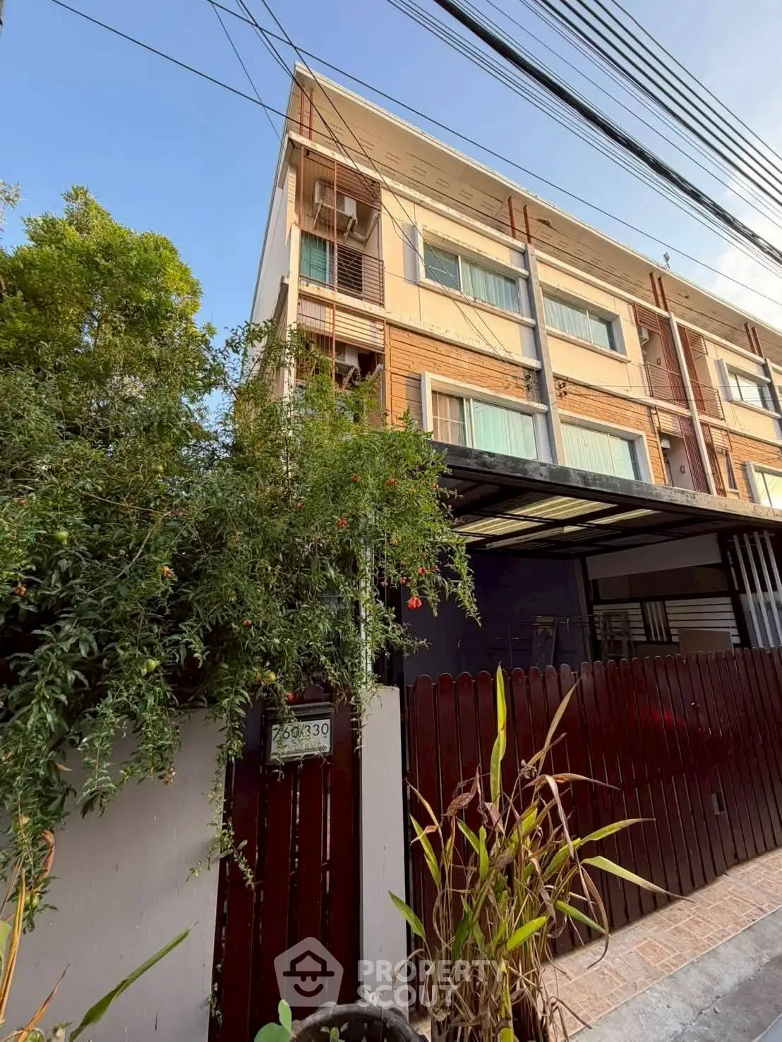 Modern multi-story building with lush greenery and wooden fence, ideal for urban living.
