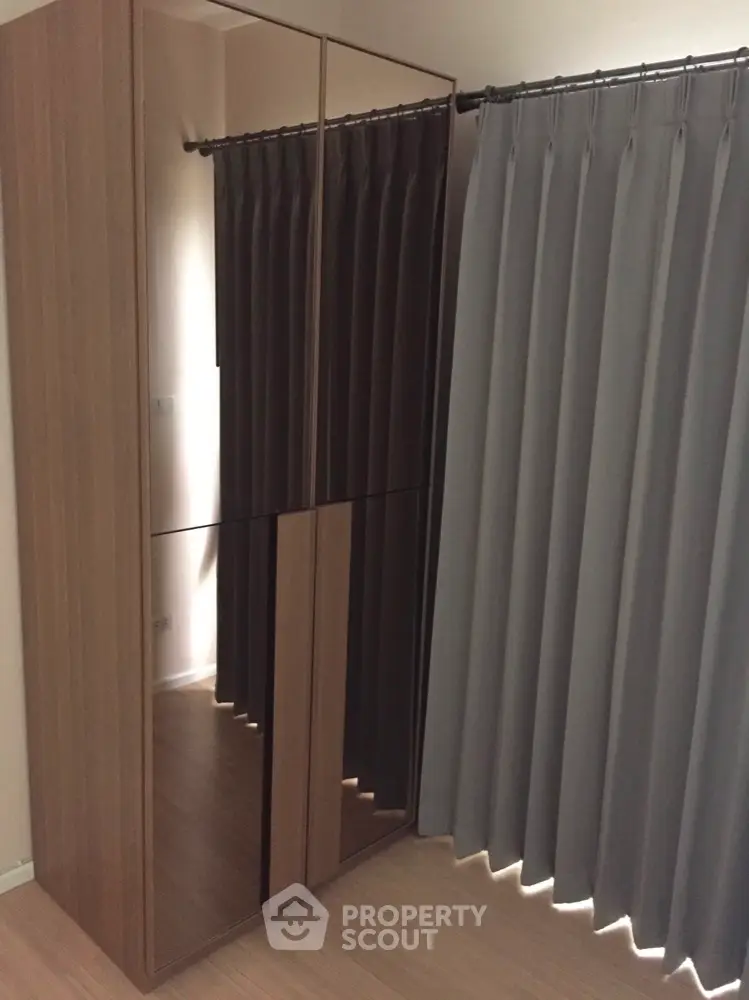 Modern minimalist bedroom with sleek wooden wardrobe and elegant gray drapery, offering a serene and organized living space.