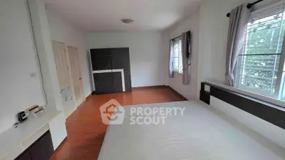 Spacious bedroom with large window and wooden flooring in modern home.