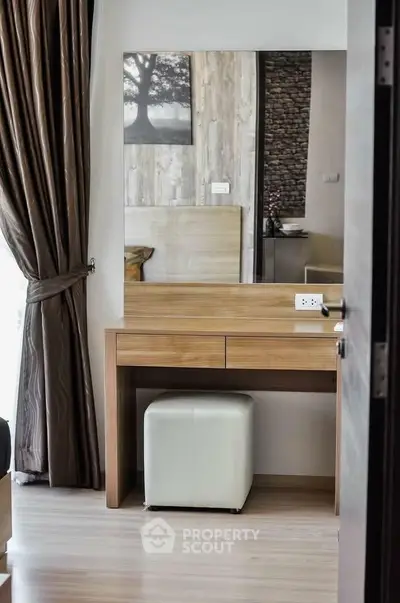 Modern bedroom with elegant wooden vanity and plush stool, featuring stylish decor and natural light.