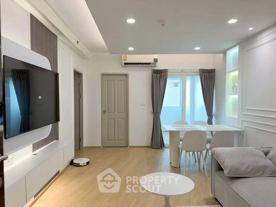 Modern living room with sleek furniture and natural light, featuring a wall-mounted TV and elegant dining area.
