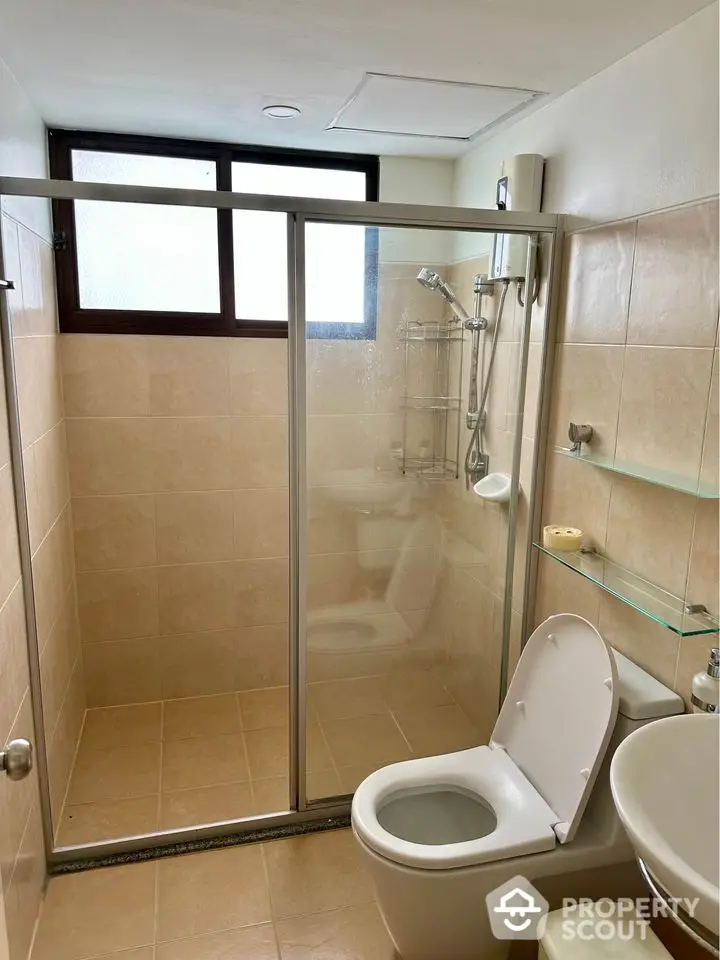 Modern bathroom with glass shower enclosure and neutral tiles.