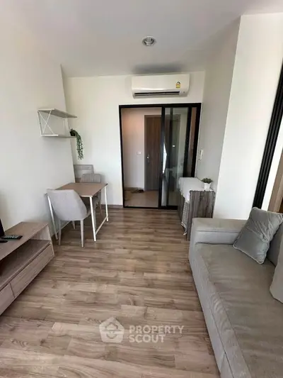 Modern living room with sleek furniture and wooden flooring, featuring a cozy workspace and air conditioning.