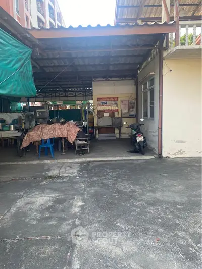 Covered outdoor area with seating and motorcycle, adjacent to a building, ideal for versatile use.