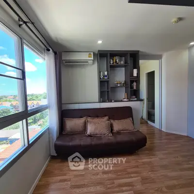 Bright living room with large window and modern decor, featuring a cozy sofa and wooden flooring.