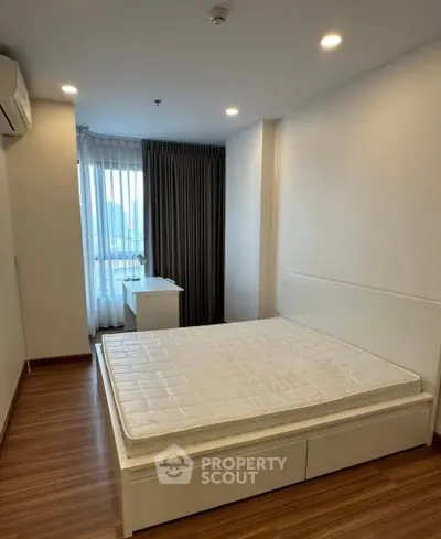 Modern bedroom with wooden flooring and large window offering city views.