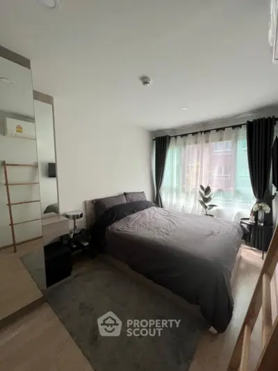 Modern bedroom with large window and stylish decor in urban apartment.