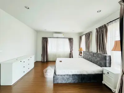 Spacious bedroom with modern furnishings and ample natural light, featuring a large bed and elegant curtains.