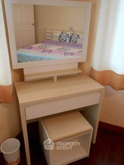 Cozy bedroom corner with stylish vanity table and mirror reflecting a neatly made bed.