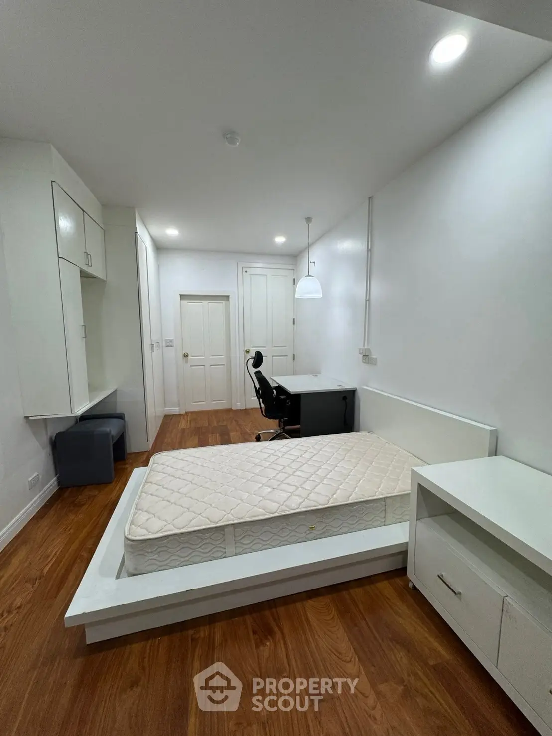 Modern bedroom with wooden flooring, built-in storage, and sleek white furniture.