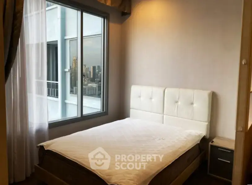 Cozy bedroom with city view, featuring a large window and modern furnishings.