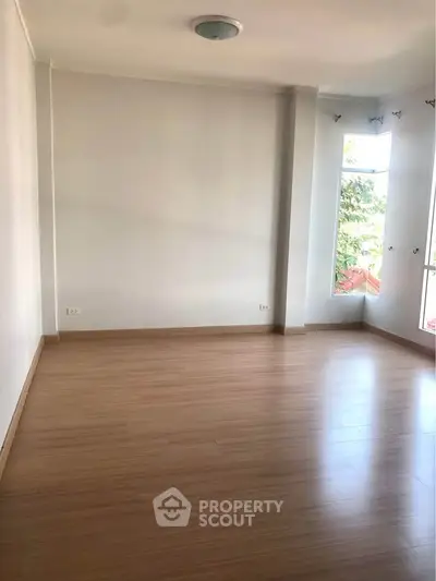 Spacious empty room with wooden flooring and large windows offering natural light.