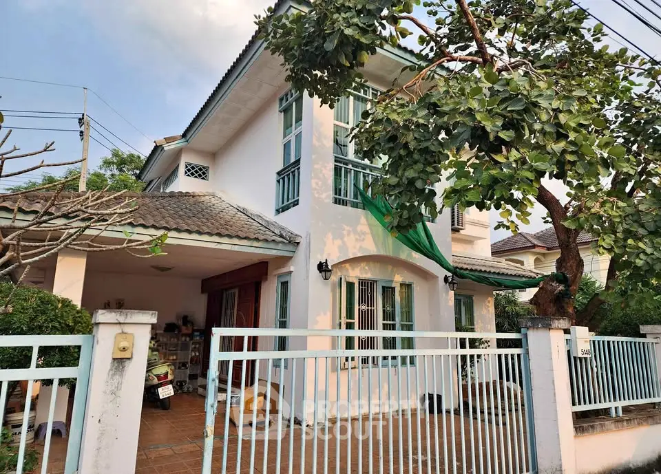 Charming two-story house with lush greenery and gated entrance, perfect for family living.
