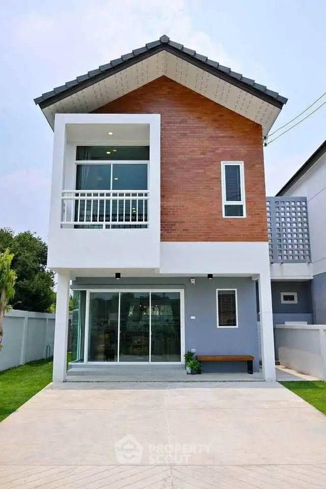 Modern two-story house with brick facade and large windows, featuring a spacious driveway and lush green lawn.