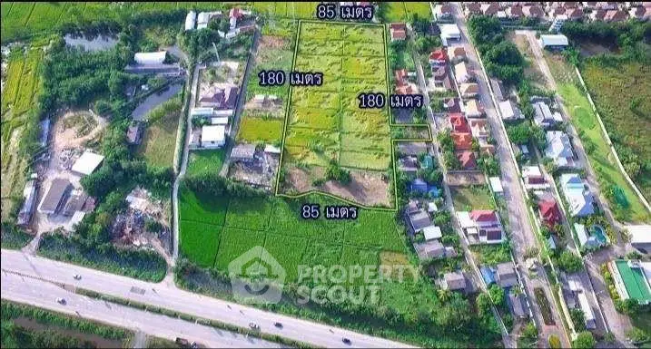 Aerial view of a residential area with plots marked for sale, showcasing lush greenery and nearby road access.