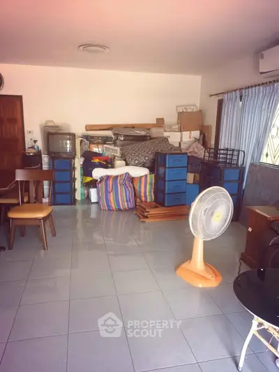 Spacious living room with tiled floor and ample storage space, featuring a fan and natural light.