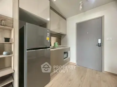 Modern kitchen with sleek cabinetry and stainless steel fridge in compact apartment.