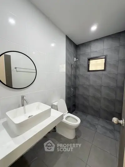 Modern bathroom with sleek design, featuring a round mirror, white sink, and gray tiled shower area.