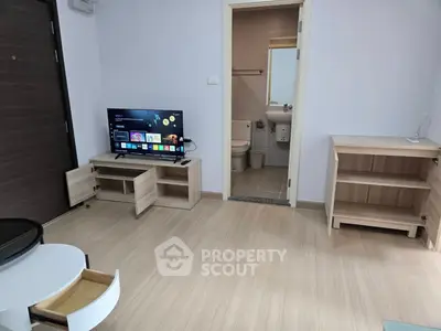 Modern living room with wooden flooring, TV setup, and view into a compact bathroom.