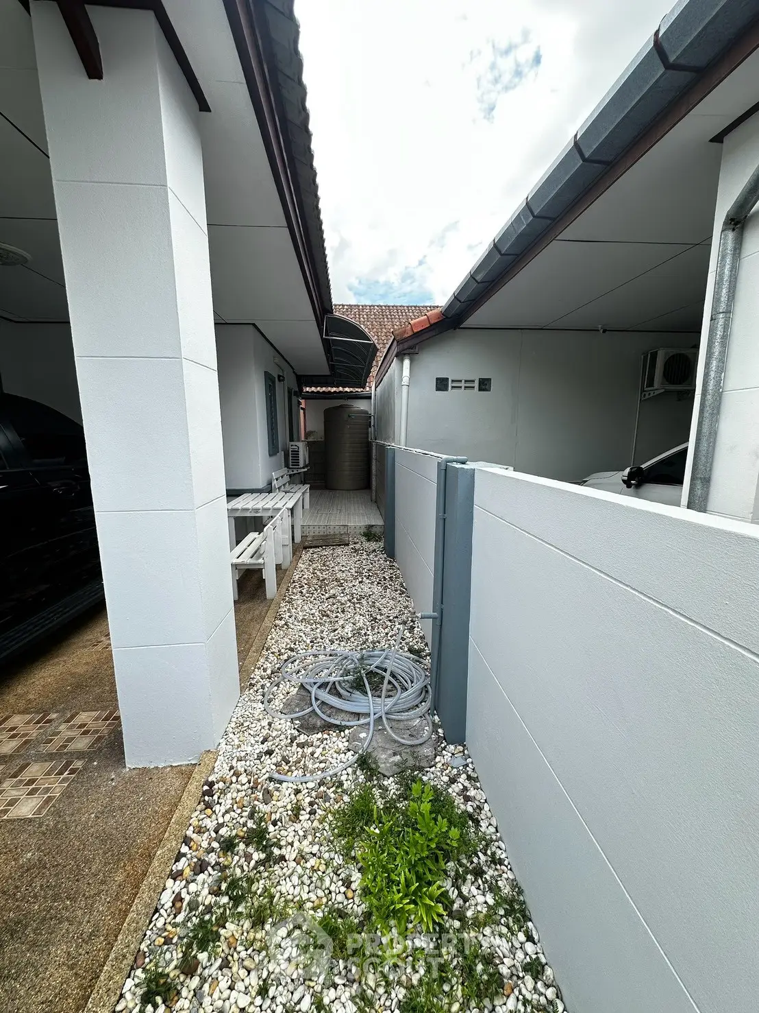 Charming side pathway with pebbled landscaping between modern homes, showcasing outdoor utility area.