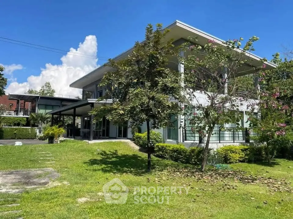 Modern two-story house with lush garden and large windows under a clear blue sky.