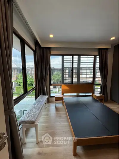 Spacious bedroom with large windows offering a serene view, featuring modern wooden furniture and elegant curtains.