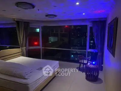 Luxurious bedroom with stunning city view and ambient lighting, featuring a cozy seating area and elegant decor.