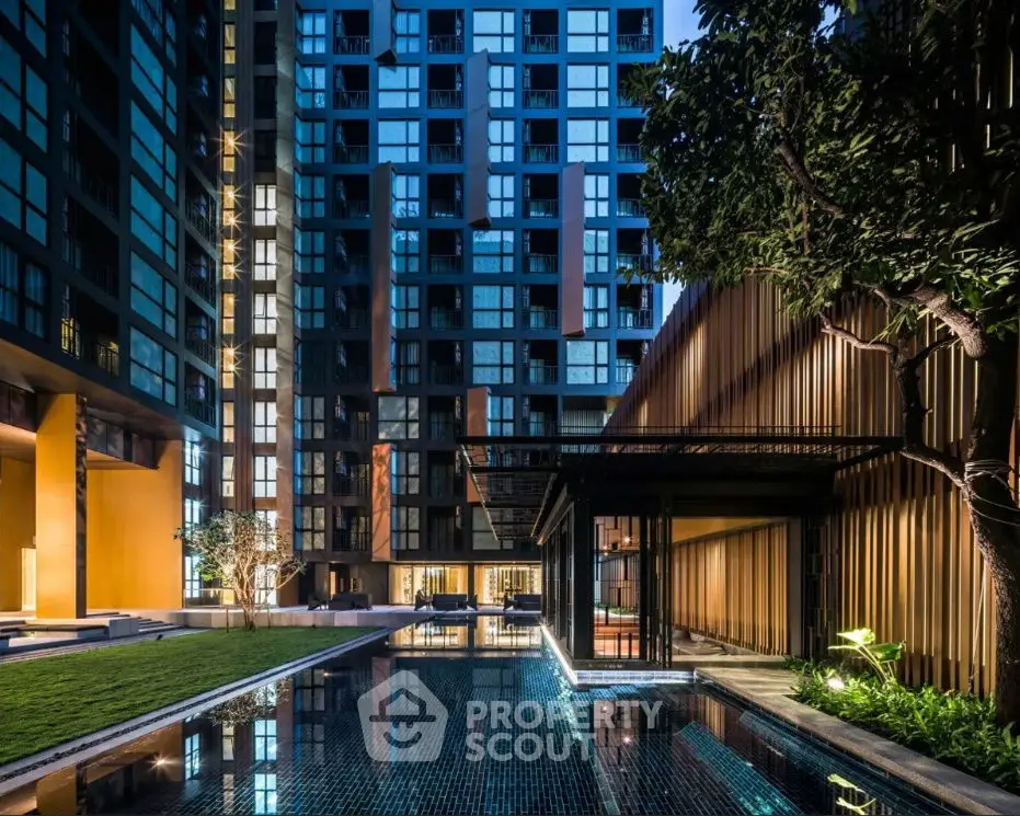 Luxurious modern apartment building with illuminated pool and lush greenery at dusk.