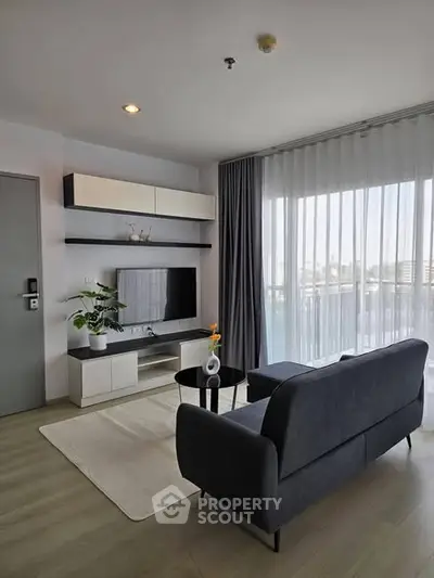 Modern living room with sleek furniture and large window offering natural light.
