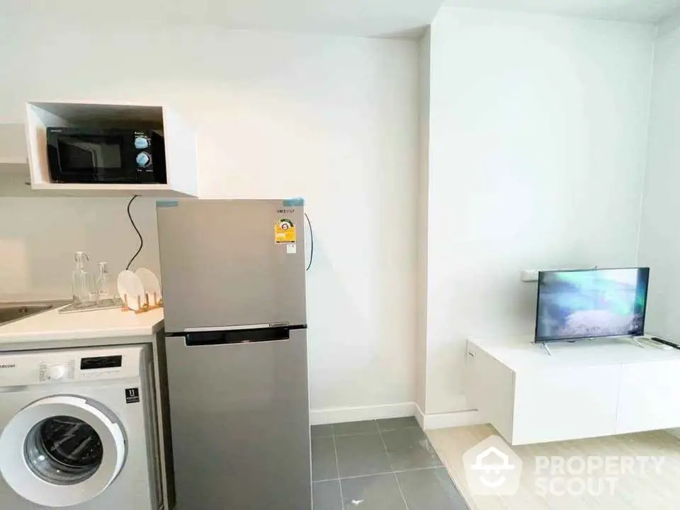 Modern compact kitchen with appliances including fridge, microwave, and washing machine in a sleek apartment.