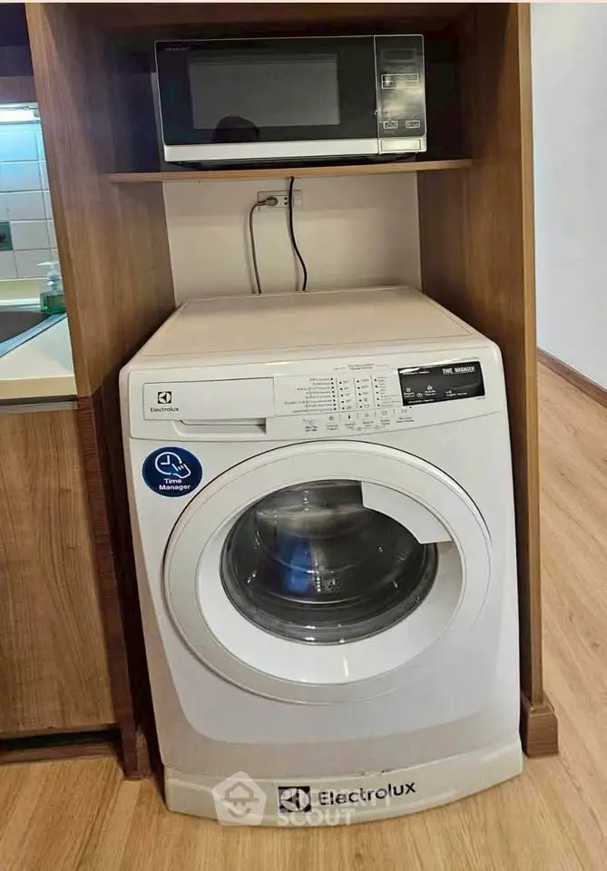 Modern laundry area with Electrolux washing machine and microwave in wooden cabinetry.
