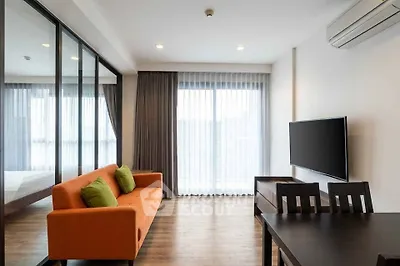 Modern living room with orange sofa, glass partition, and wall-mounted TV in a bright apartment.