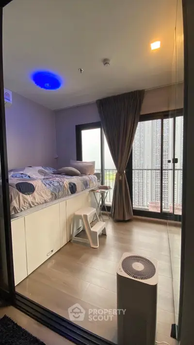 Modern bedroom with elevated bed and large window offering natural light and city view.