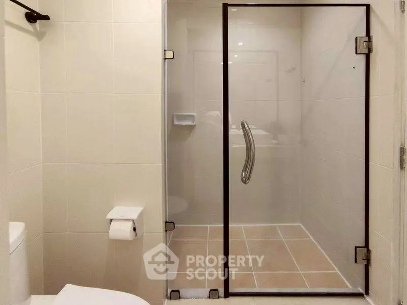 Modern bathroom with glass shower enclosure and tiled walls.