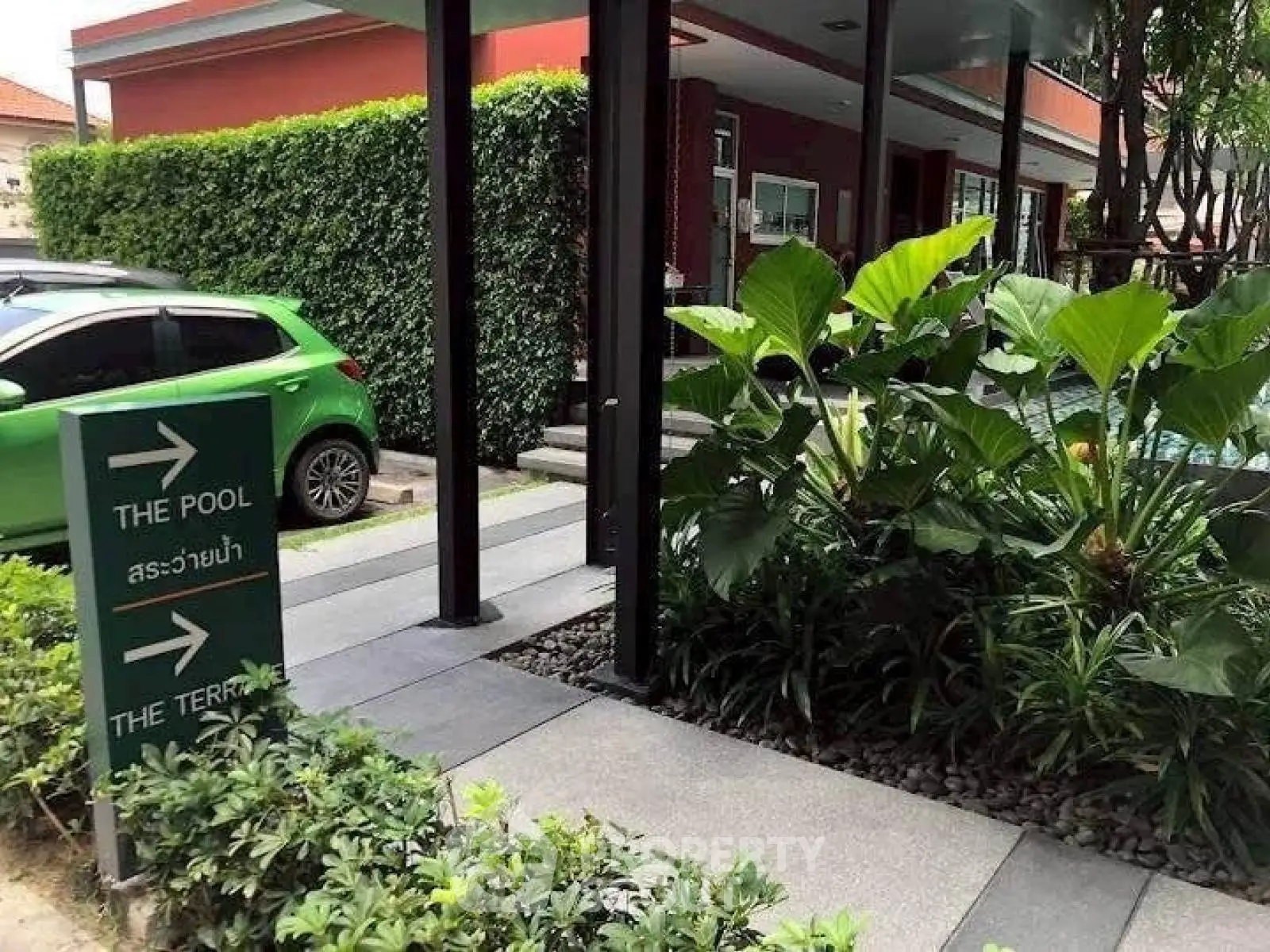 Modern building entrance with lush greenery and pool access signage.